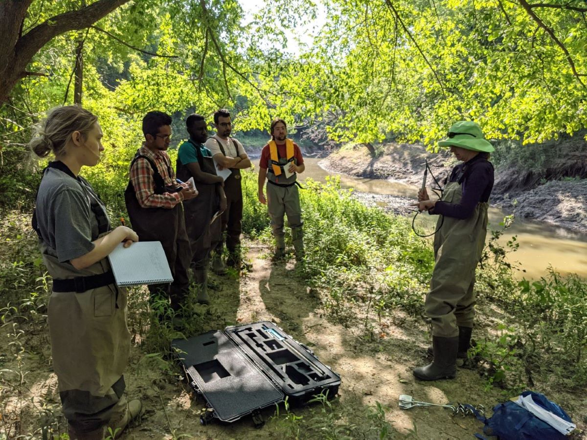 Students listening to instructor outside next to a river