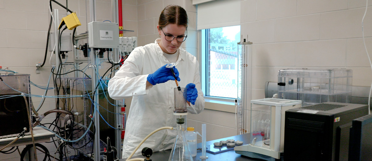 A student in a lab using a vial in a beaker